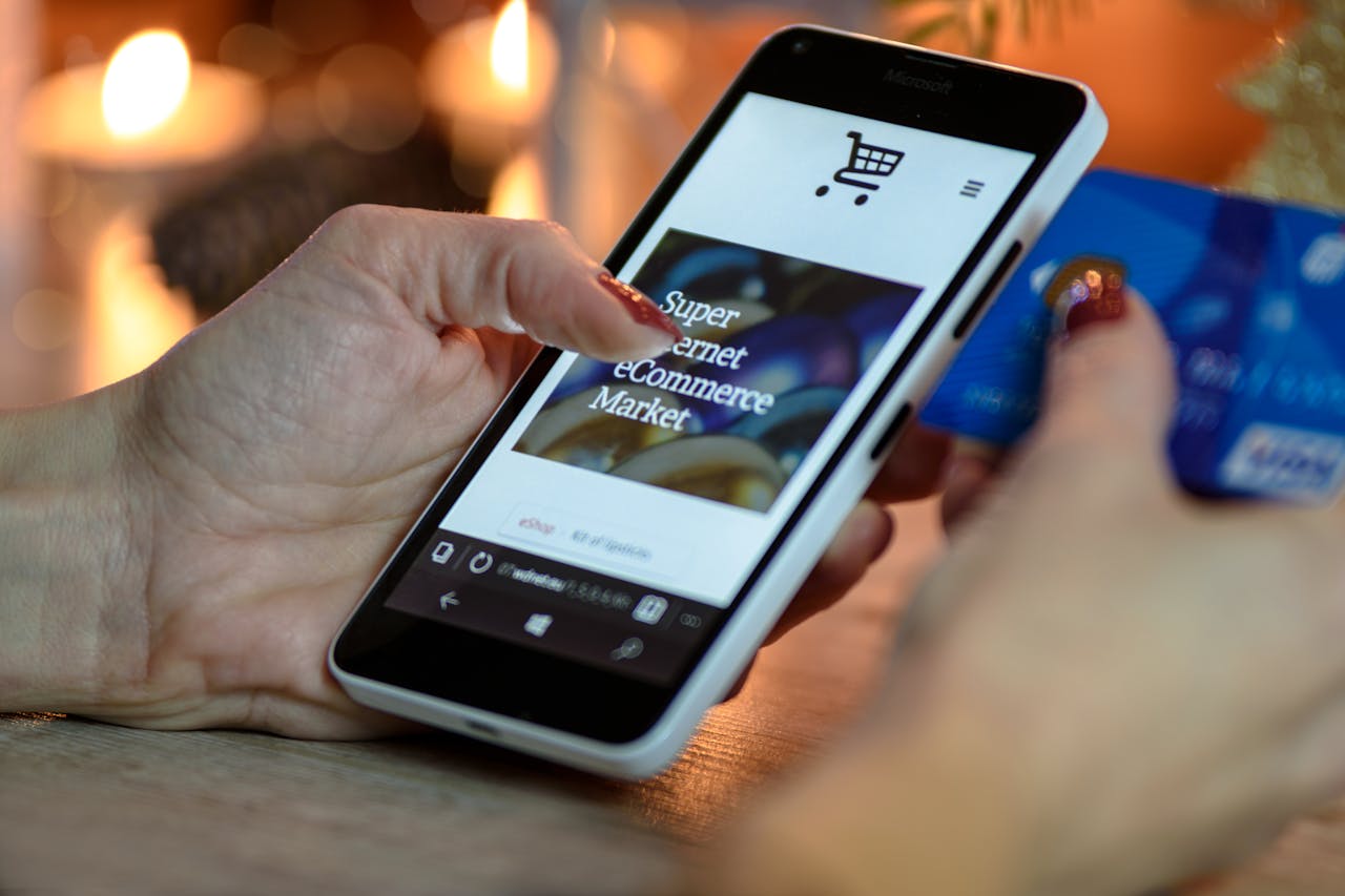 about-01 Woman using smartphone for online shopping with credit card in hand, festive background lighting.